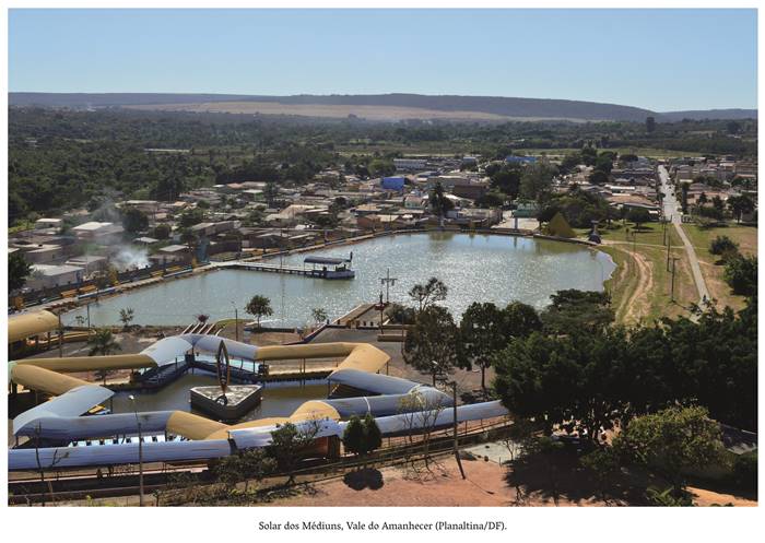  4 n- Solar dos Médiuns, Vale do Amanhecer Planaltina- DF O solar é colorido onde vê-se um triângulo amarelo e azul na entrada. Ao centro um lago com águas límpidas e ao fundo várias casas próximas as outras. Realização: Academia Planaltinense de Letras, Artes e Ciências (APLAC), pelo Ecomuseu Pedra Fundamental e pelo Coletivo Nativo Audiodescrição produzida  pelo Instituto de Promoção das Pessoas com Deficiência Visual Audiodescritora: Elma Lúcia Rodrigues Consultor: Fernando Rodrigues Este projeto é promovido com recursos do Fundo de Apoio a Cultura do DF